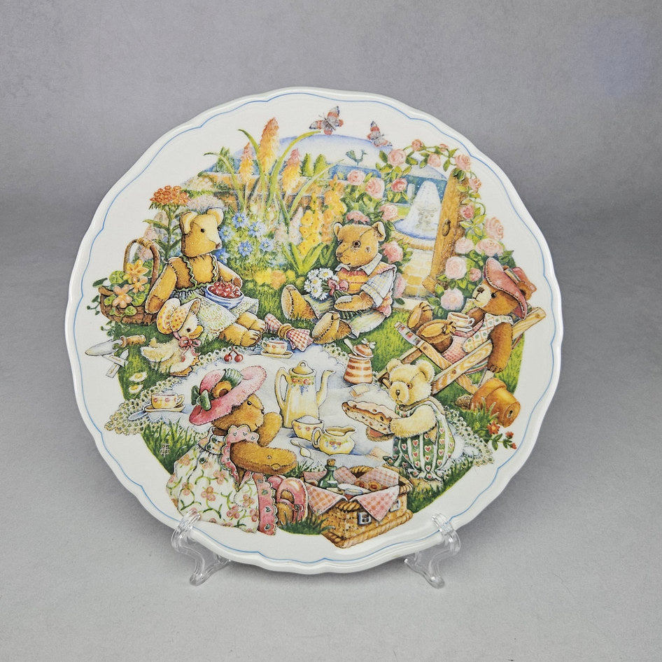 Royal Albert Teddy Bear Tales The Picnic bone china collector plate displayed on a clear plate stand, featuring a detailed storybook scene of teddy bears enjoying a garden picnic with tea wares and flowers
