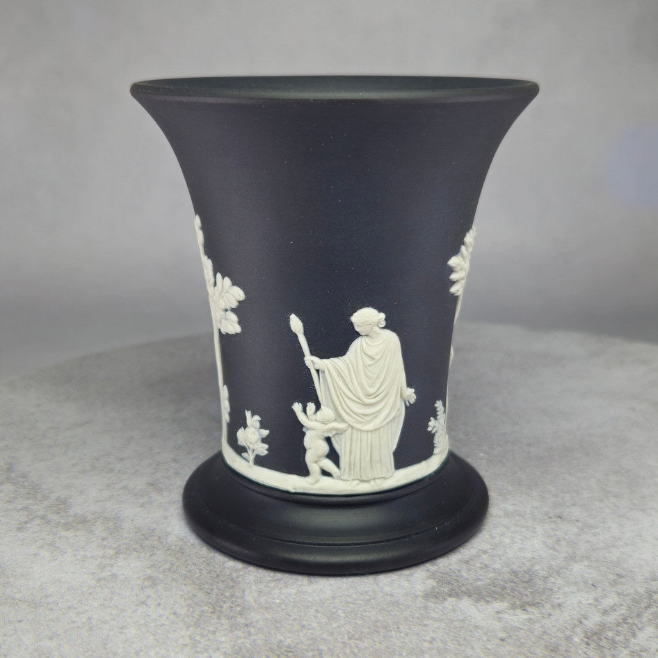 Wedgwood black Jasperware trumpet vase with white neoclassical relief figures including a classical figure and cherub on a matte black ground, displayed on a grey surface