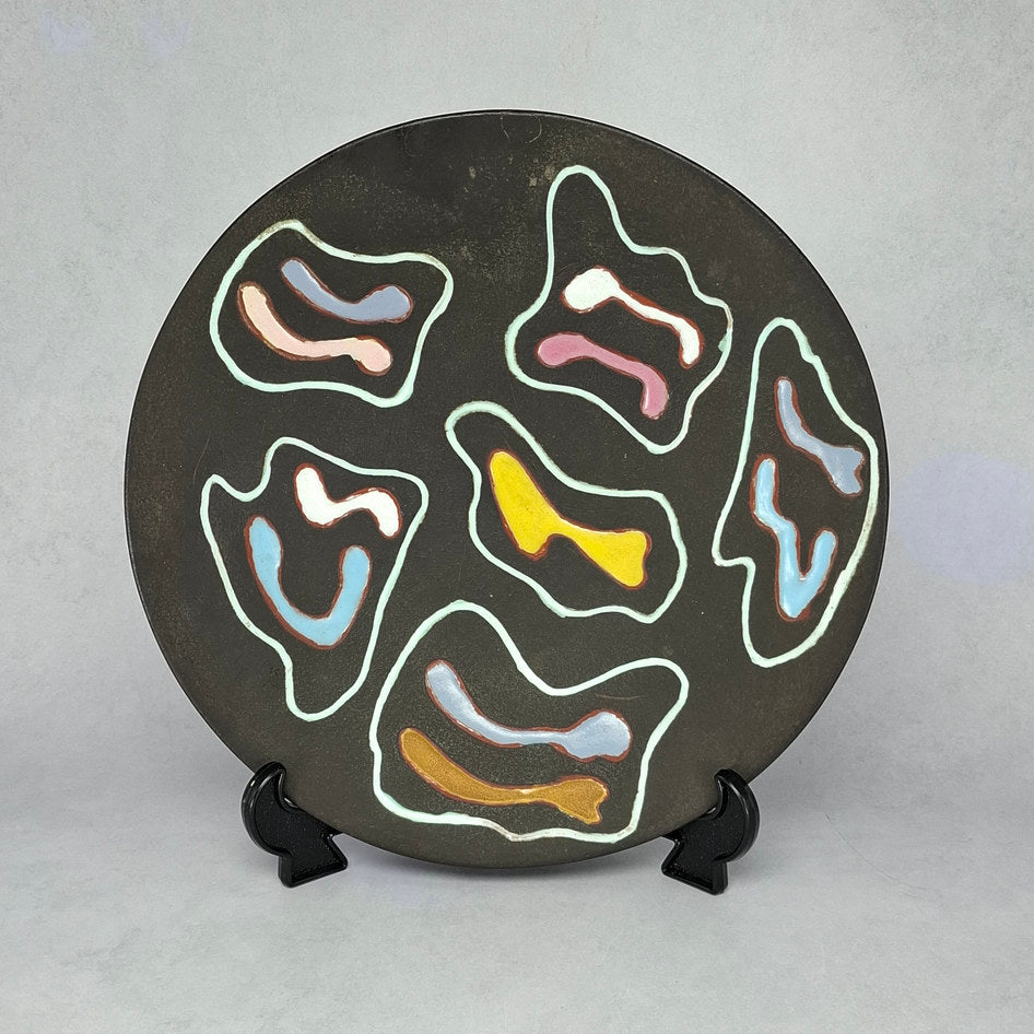 South African mid-century studio ceramic plate with abstract multicolour enamel motifs on dark ground, displayed on a plate stand