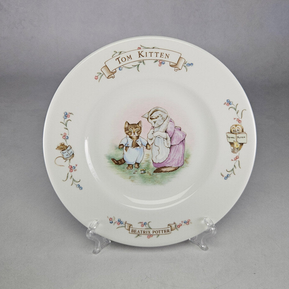 Royal Albert The World of Beatrix Potter Tom Kitten bone china plate displayed on a clear plate stand, showing Tom Kitten and Mrs Tabitha Twitchit with character name banners and floral border detail
